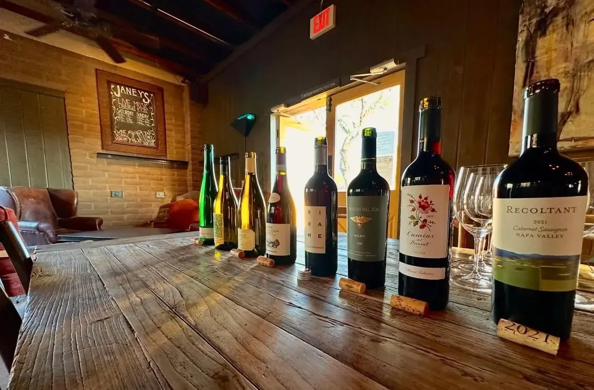 Wine bottles and glasses arranged along a wooden table inside Janey’s