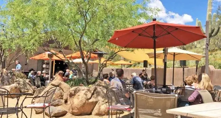Guests gathered beneath colorful umbrellas among desert trees and rocks on Janey’s patio