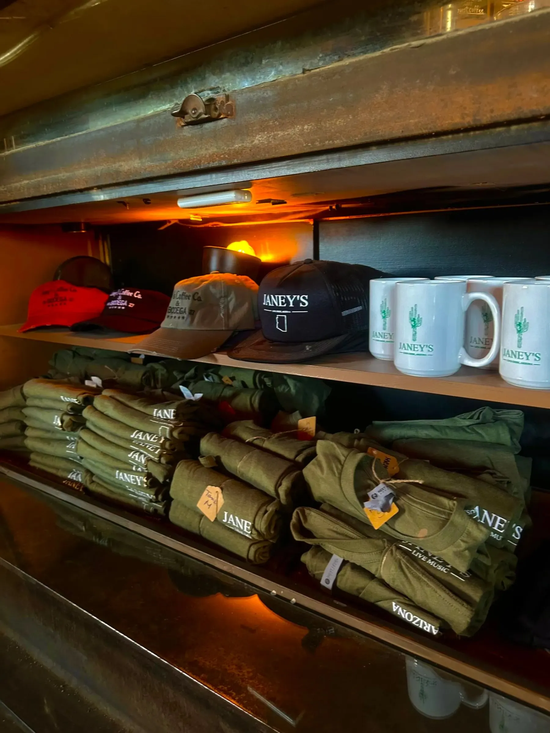 Janey’s branded hats, mugs, and folded shirts displayed on wooden shelves
