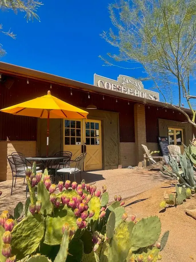 Janey’s Coffee House entrance, with its sign, yellow patio umbrella, and desert plants