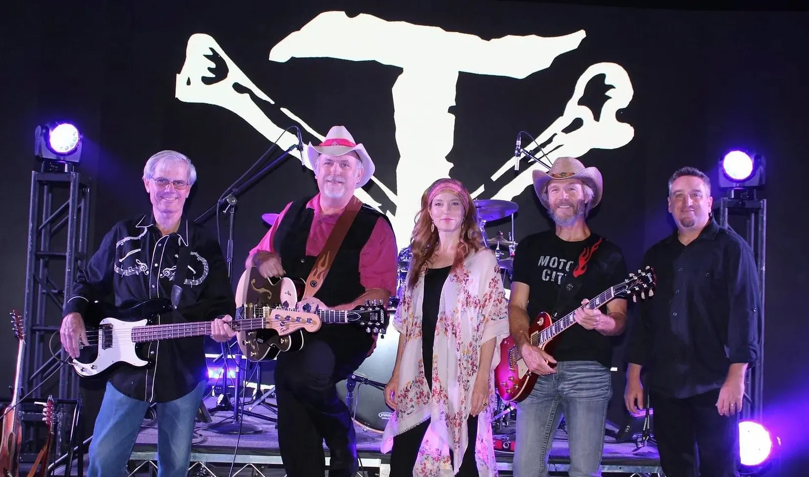 The T-BoneZ: five musicians posing on a stage with guitars and a drum kit